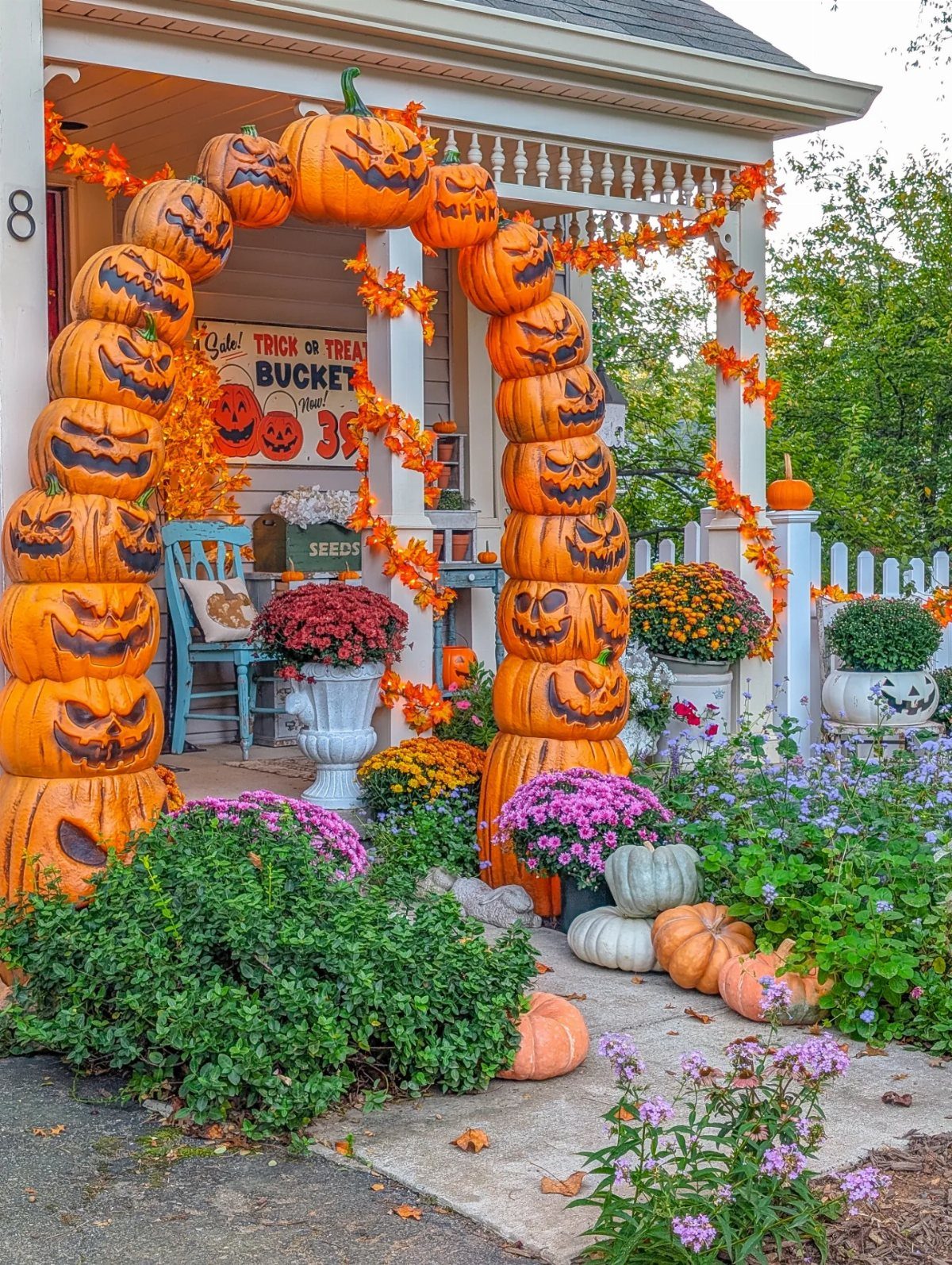 14 Front Porch Decorating Ideas for Every Season 13 An archway of stacked jack-o'-lanterns decorates a front porch with autumn flowers and pumpkins.