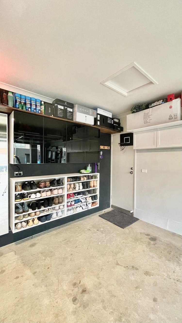 9 Garage Storage Shoes For Any Budget, Wall to Floor 5 White built-in shoe shelves filled with many pairs of shoes against a dark wall.