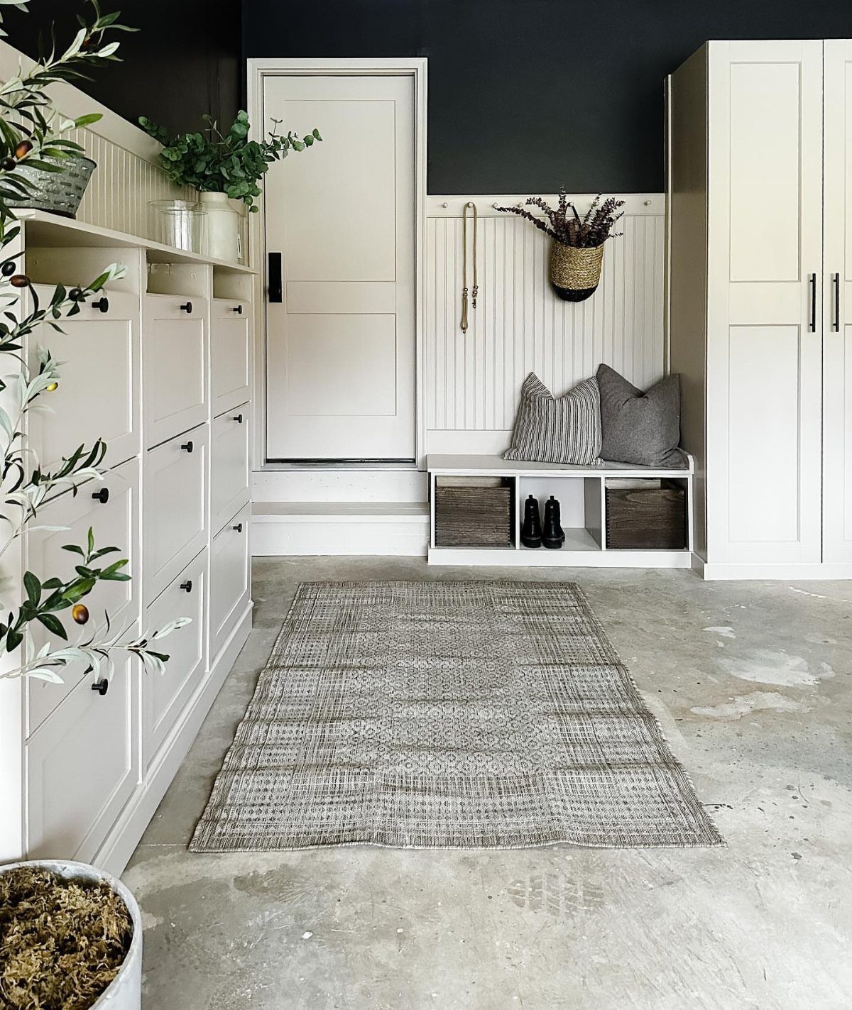 9 Garage Storage Shoes For Any Budget, Wall to Floor 3 White built-in shoe storage bench with pillows and shoes in cubbies against a dark wall.