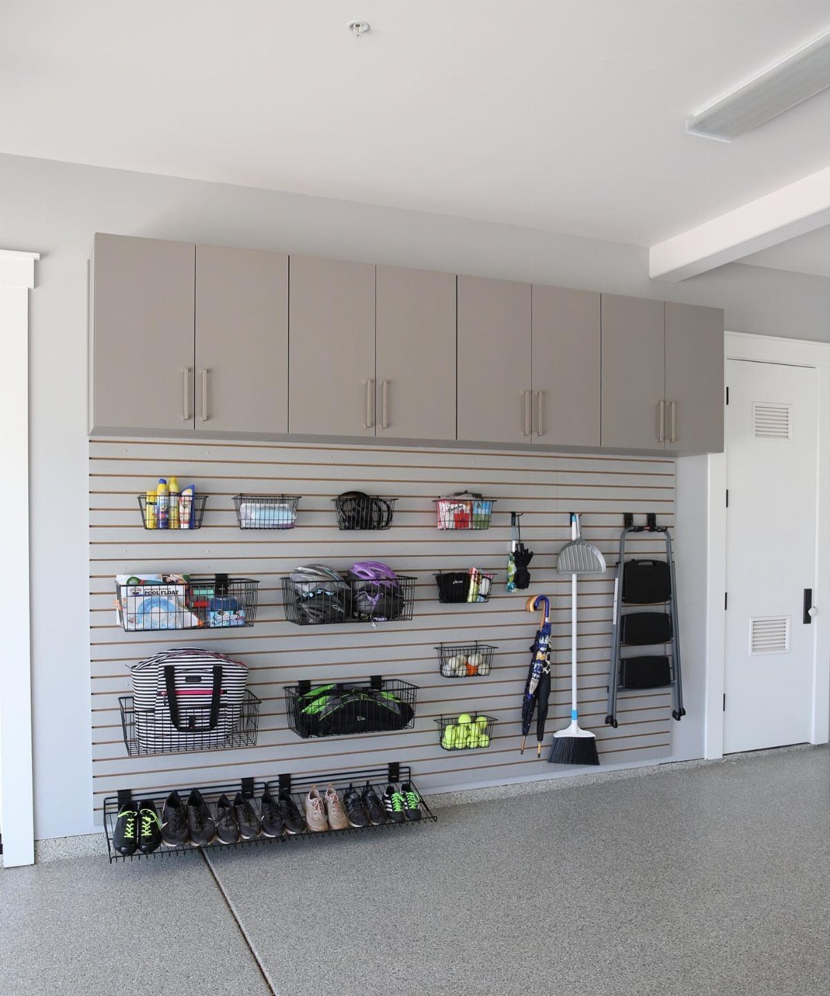9 Garage Storage Shoes For Any Budget, Wall to Floor 1 Slatwall organization system in a garage with baskets, hooks, and shoes on the floor.