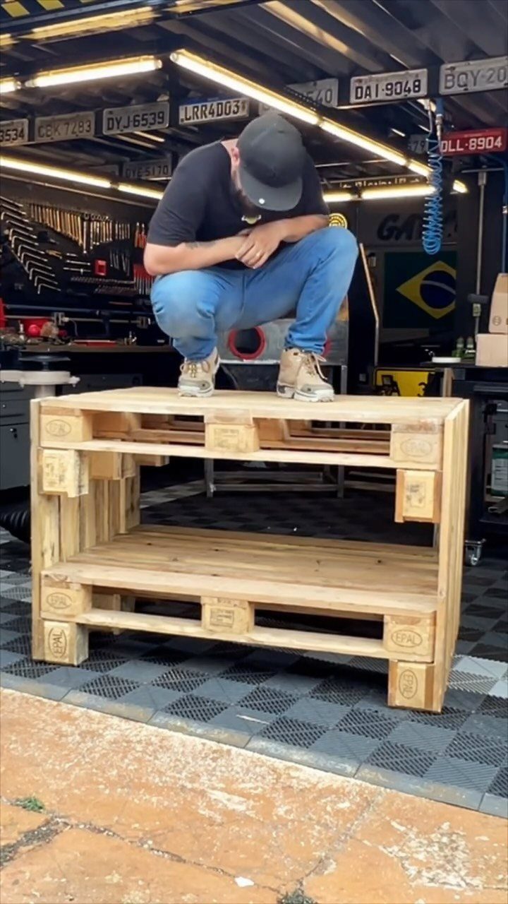 Garage Storage Using Pallets: 5 Projects for Vertical Racks and Tool Cubbies 5 A man sitting on a large storage shelf made from wooden pallets in a workshop.