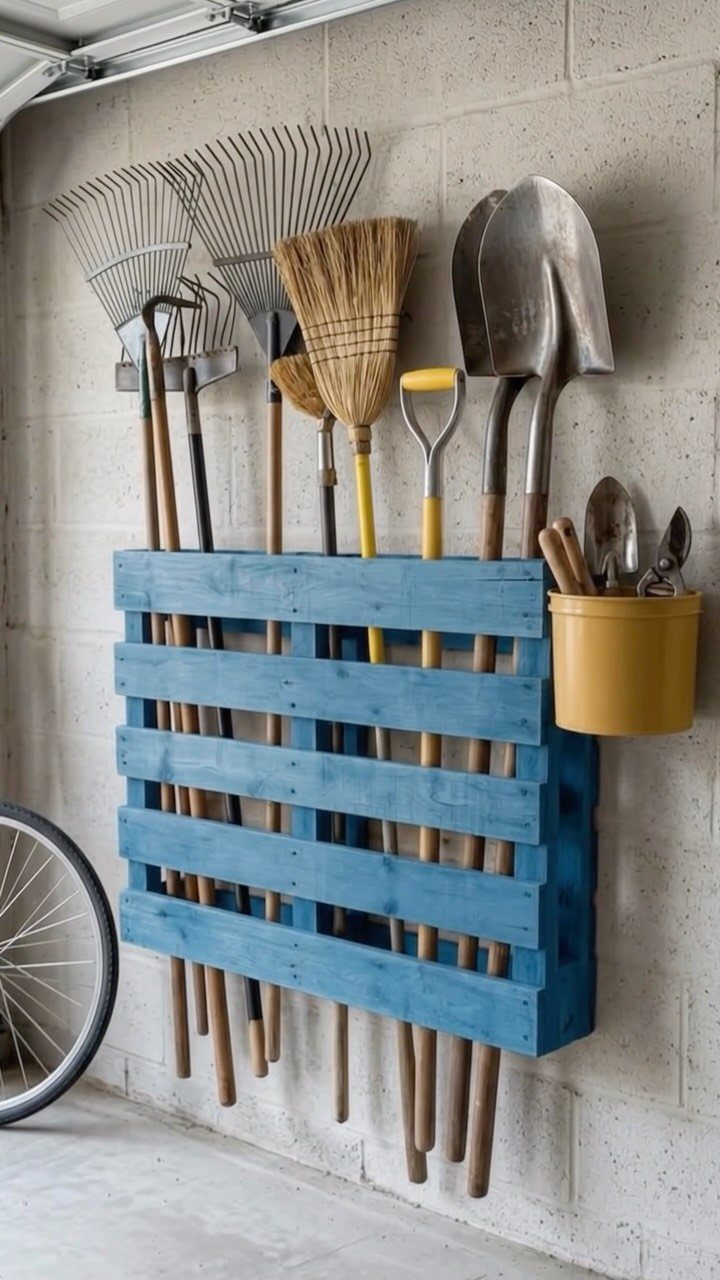 Garage Storage Using Pallets: 5 Projects for Vertical Racks and Tool Cubbies 2 Blue painted pallet mounted on a wall holding various garden tools like rakes and shovels.