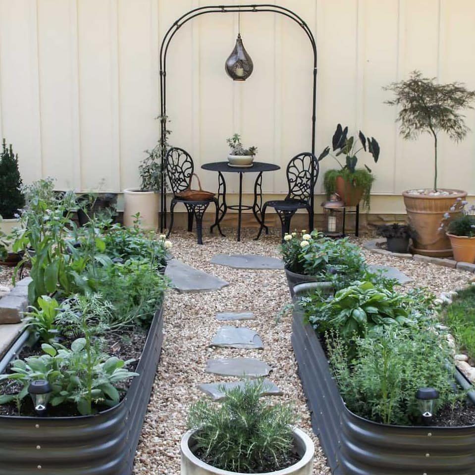 Two galvanized steel raised beds filled with lush green herbs on a gravel patio.