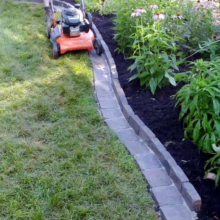 Grey stone pavers create a clean edge between a green lawn and a dark mulch garden bed.