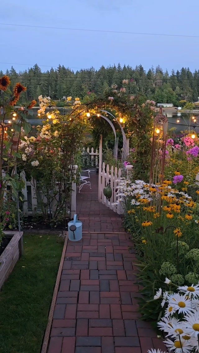 A brick garden path winding through blooming flowers and a rose-covered archway.