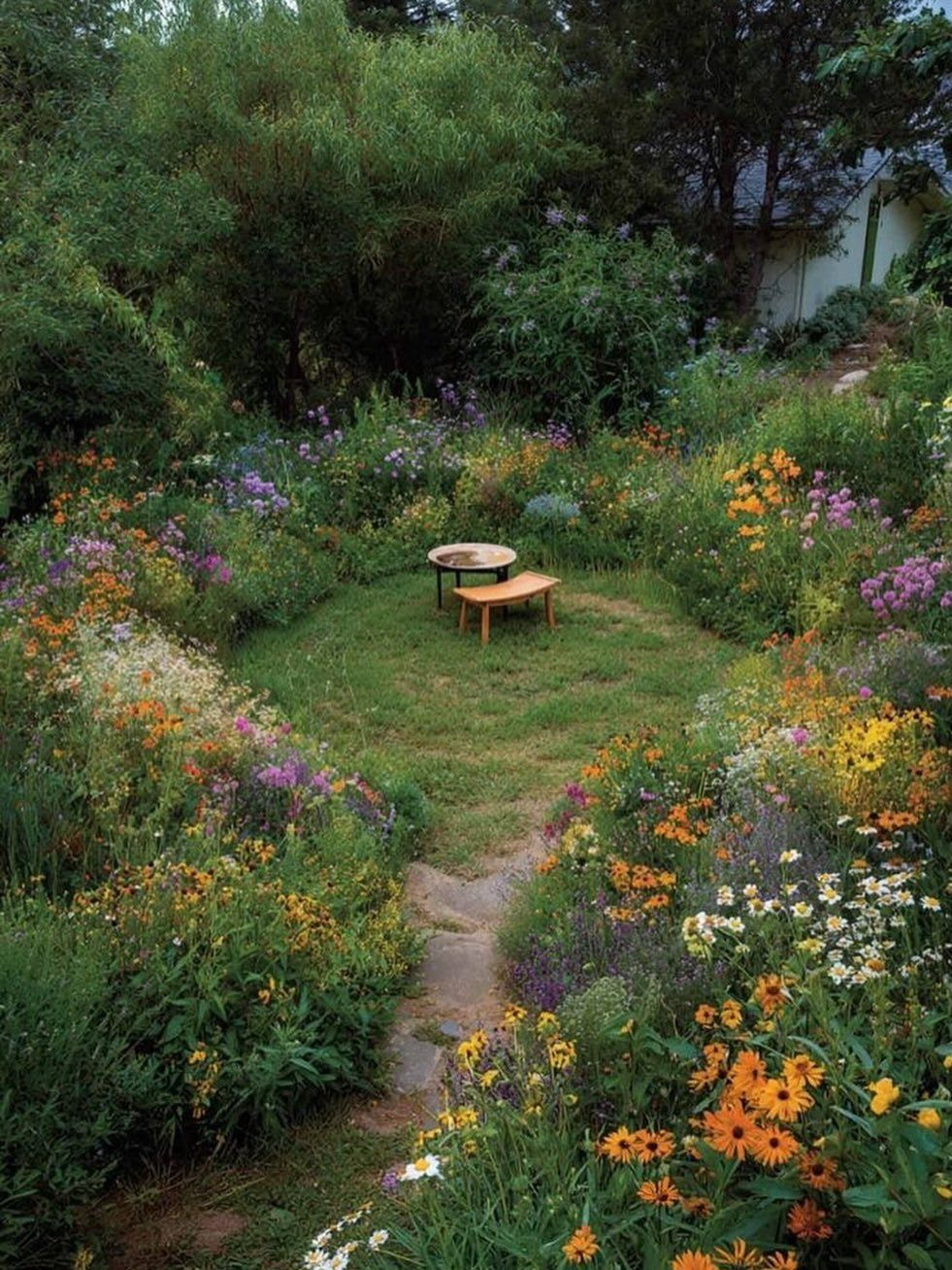 Wildflowers in orange, yellow, and purple bloom densely around a small grassy area with a wooden bench.