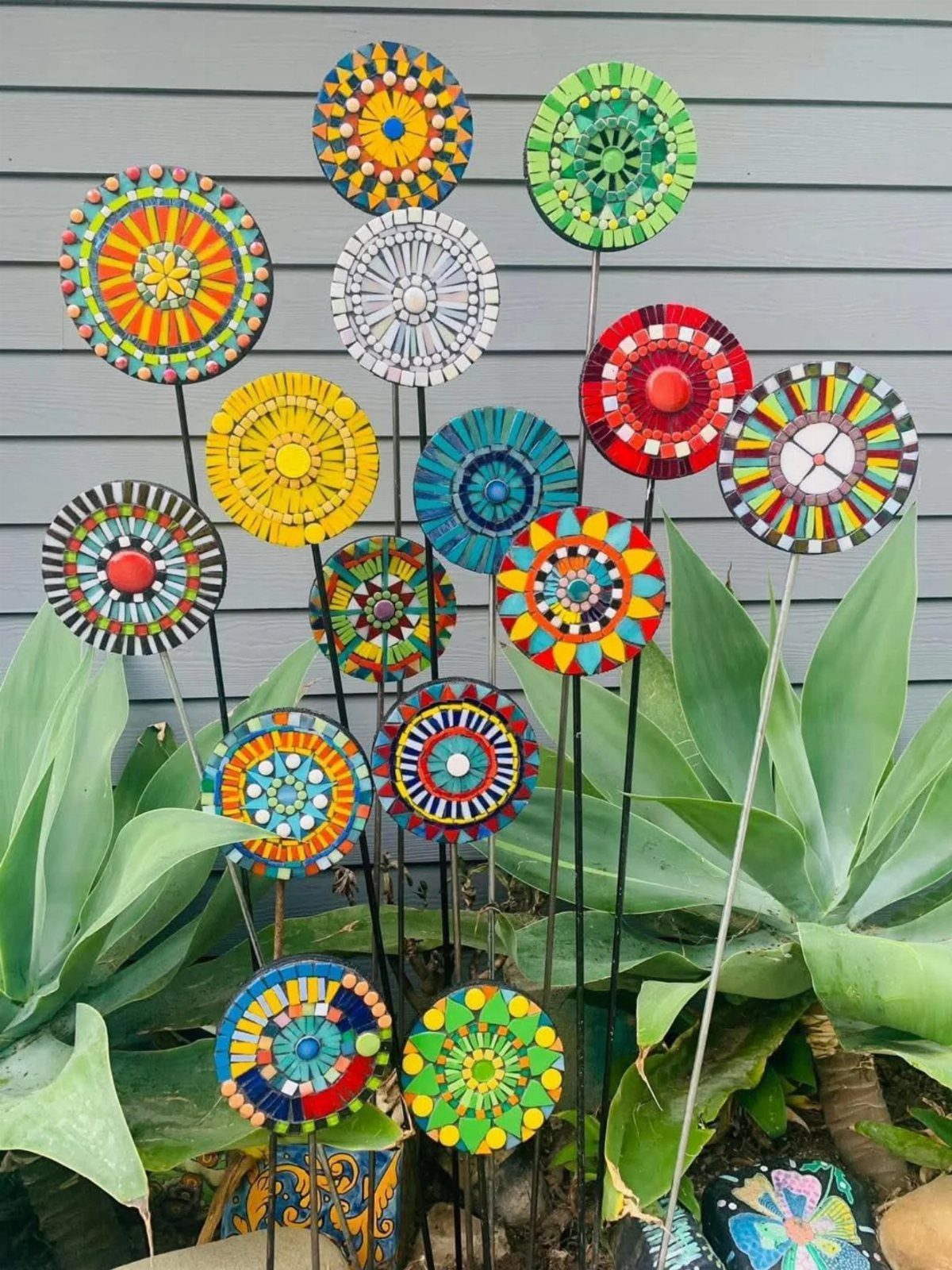 Colorful mosaic disc garden stakes planted among large green succulent plants in a garden.