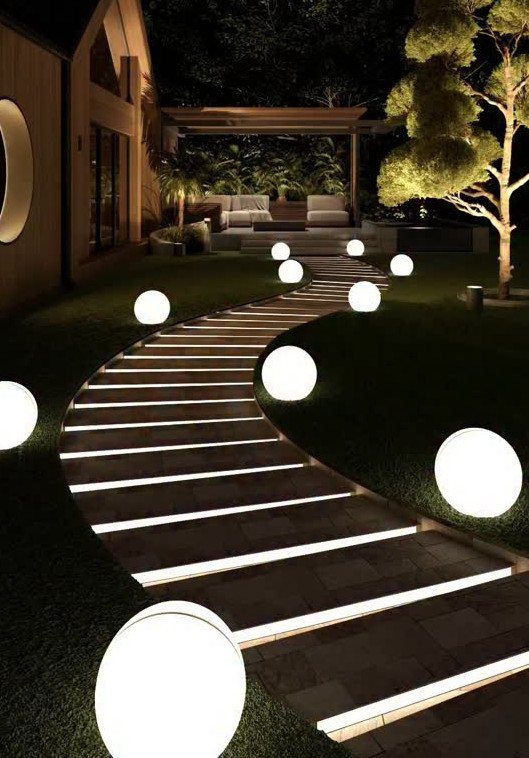 Glowing white orb lights line a winding stone path through a dark garden lawn.