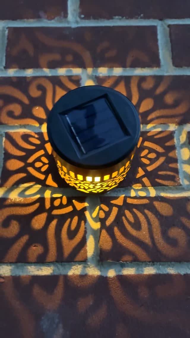Solar lantern glowing on red bricks, casting decorative light patterns across the patio surface.