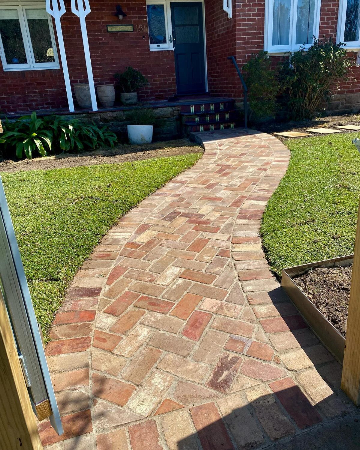 10 Garden Pathways Ideas for Gravel, Brick, Wood and Stone 3 A curved brick pathway with a herringbone pattern winding through a green grass lawn.