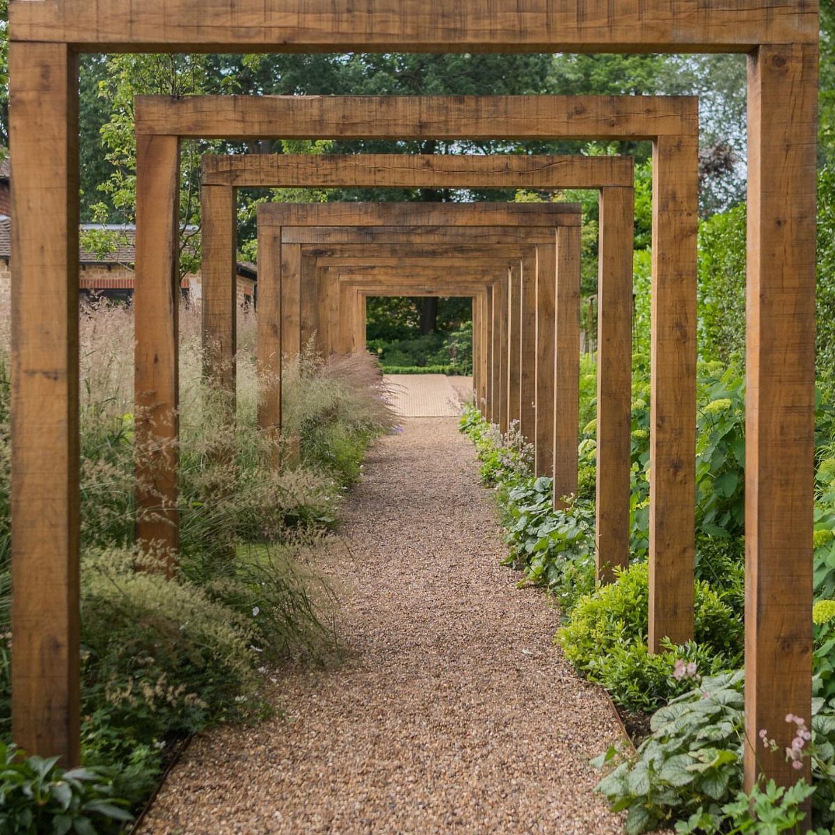10 Garden Pathways Ideas for Gravel, Brick, Wood and Stone 1 A gravel garden path lined with a series of tall, rustic wooden rectangular frames and lush green plants.
