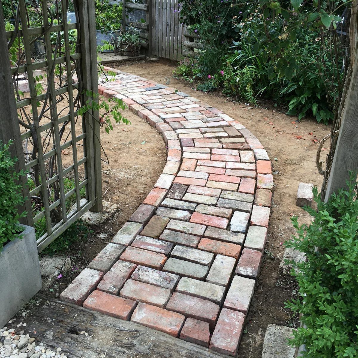 10 Garden Pathways Ideas for Gravel, Brick, Wood and Stone 9 A curved brick pathway laid in a herringbone pattern through a lush green garden.