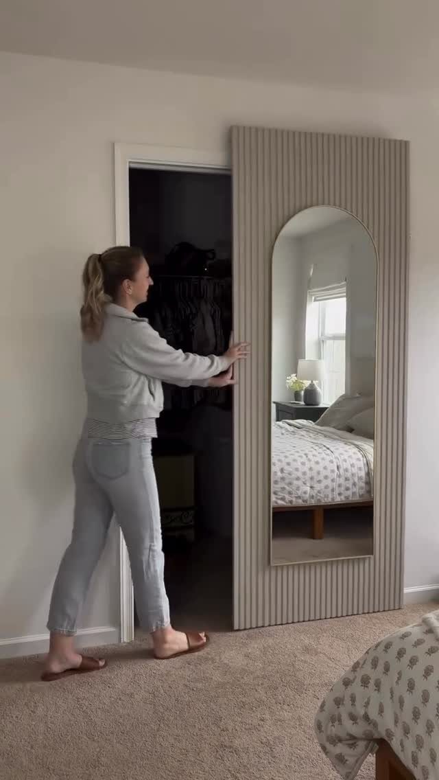 9 Hidden Storage Entrance Ideas for Bookshelf Doors and Hidden Hatches 6 A woman opens a large arched mirror to reveal a hidden closet entrance behind the panel.