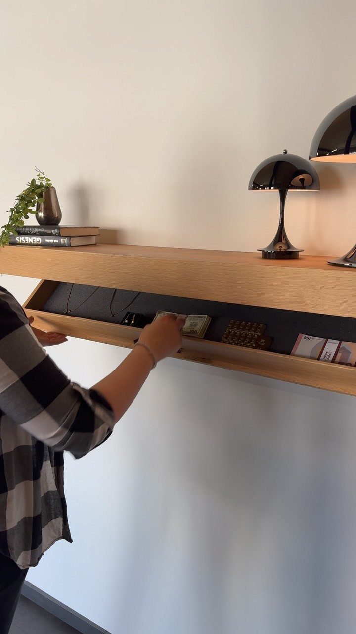 9 Hidden Storage Entrance Ideas for Bookshelf Doors and Hidden Hatches 4 A person reaching into a hidden compartment inside a long wooden floating shelf mounted on a white wall.