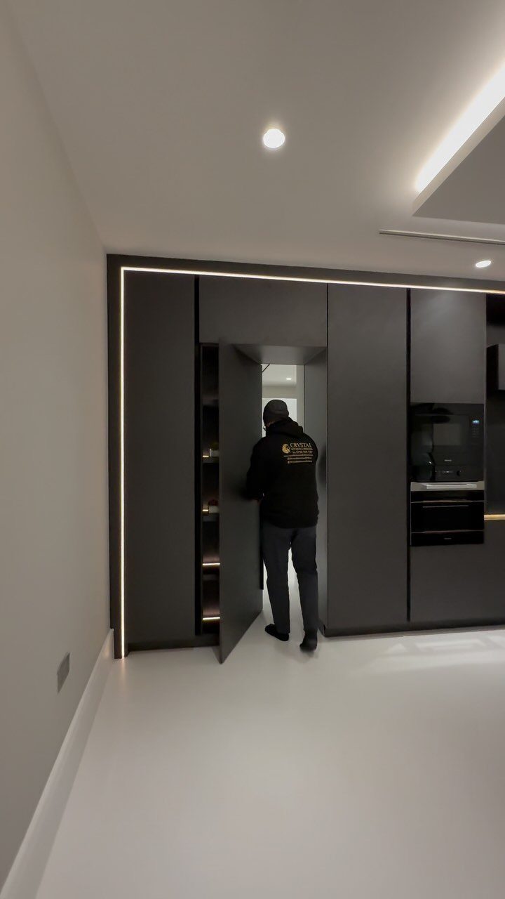9 Hidden Storage Entrance Ideas for Bookshelf Doors and Hidden Hatches 3 A person opens a large dark grey kitchen cabinet to reveal a hidden doorway behind it.
