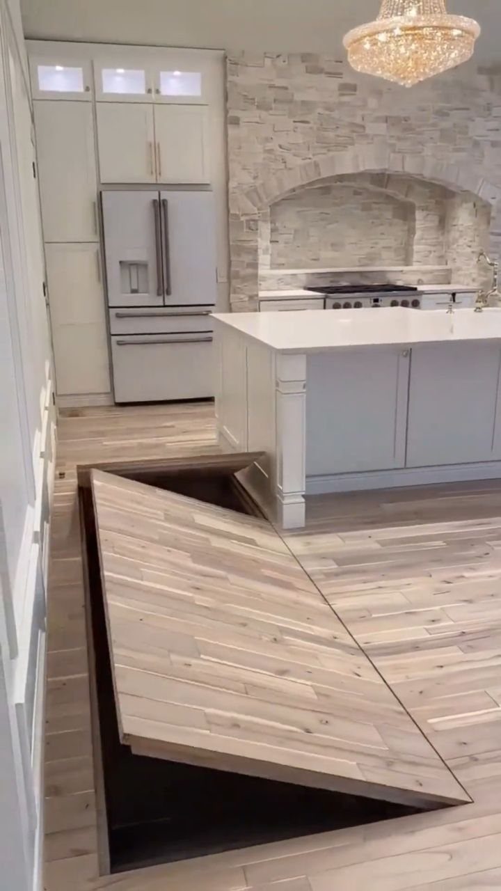 9 Hidden Storage Entrance Ideas for Bookshelf Doors and Hidden Hatches 2 A wooden floorboard lifted in a modern kitchen to reveal a dark trapdoor underneath.