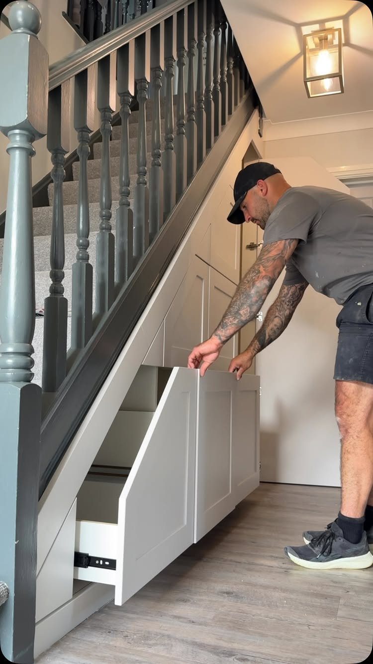 9 Hidden Storage Entrance Ideas for Bookshelf Doors and Hidden Hatches 7 A man opens a white storage drawer built into the space under a staircase.