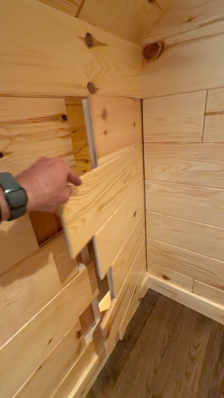 9 Hidden Storage Entrance Ideas for Bookshelf Doors and Hidden Hatches 8 A hand pulls a wooden plank away from a wall to reveal a hidden opening.