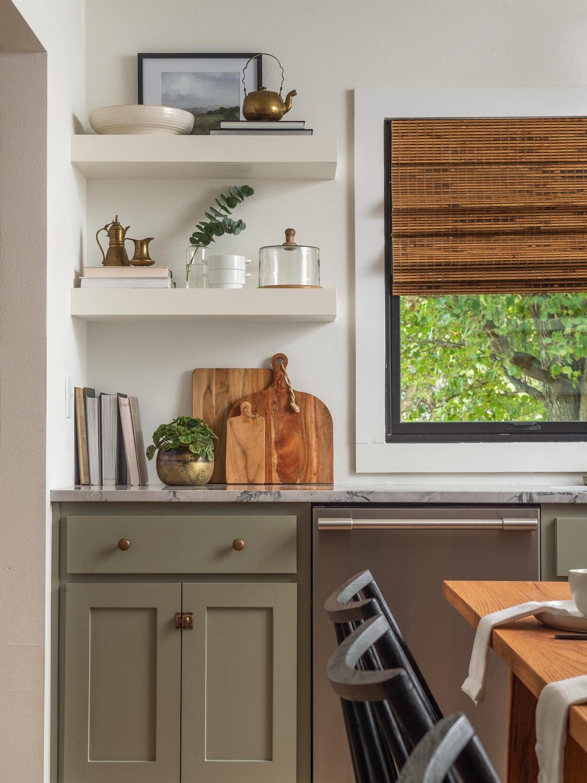 White floating shelves decorated with brass teapots, books, and greenery above a kitchen counter.