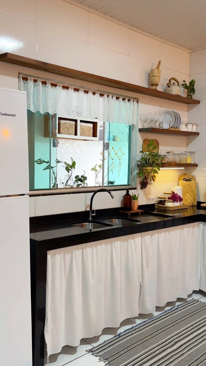 Wooden floating shelves holding white dishes and plants against a white tiled kitchen wall.