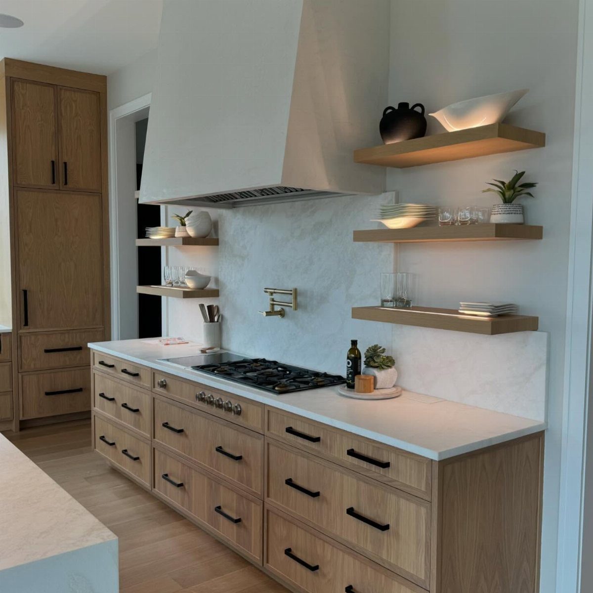Three wooden floating shelves holding white dishes and plants on a marble kitchen backsplash.