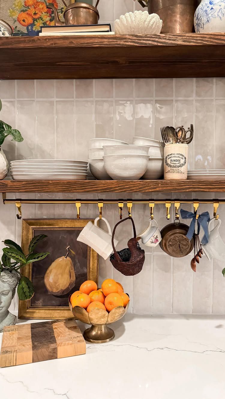 Wooden open shelves with a brass rail holding various mugs and kitchen items via gold hooks.