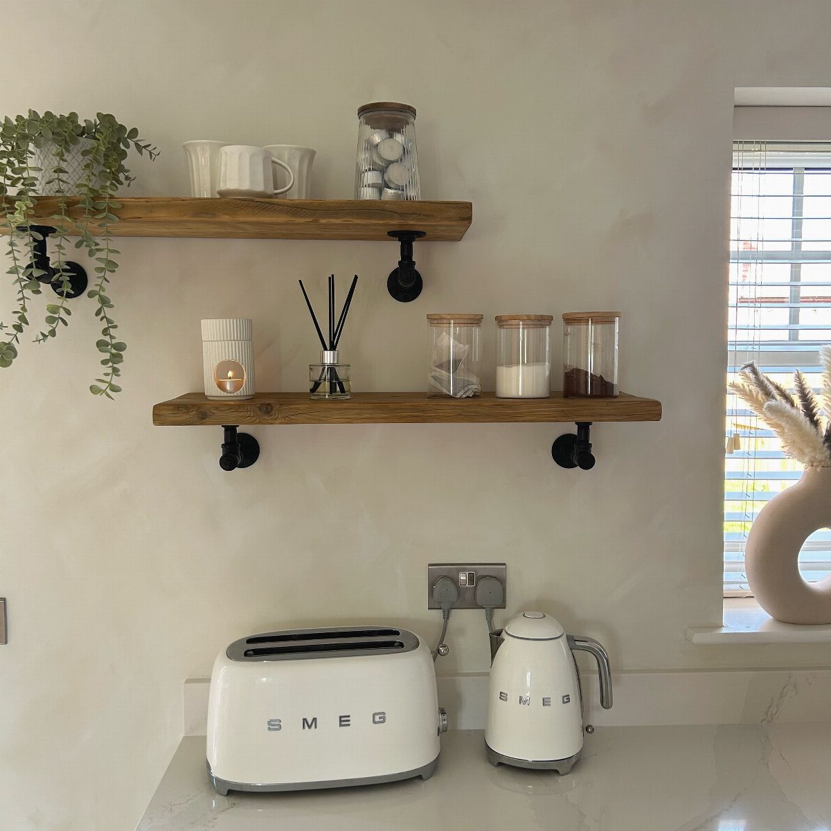 Wooden shelves with black pipe brackets holding kitchenware on a white wall above a countertop.