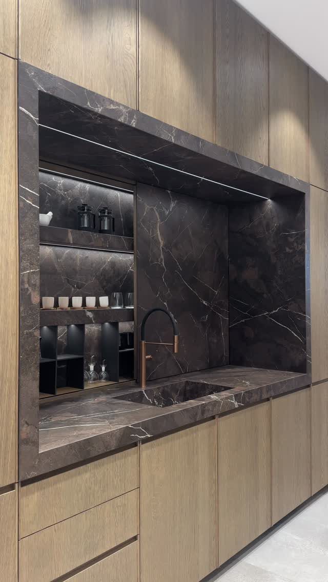 Dark marble recessed shelving and sink area built into light wood kitchen cabinetry.