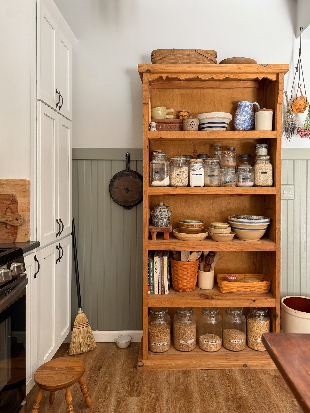 A tall wooden hutch filled with organized kitchenware, jars, and bowls against a green wall.
