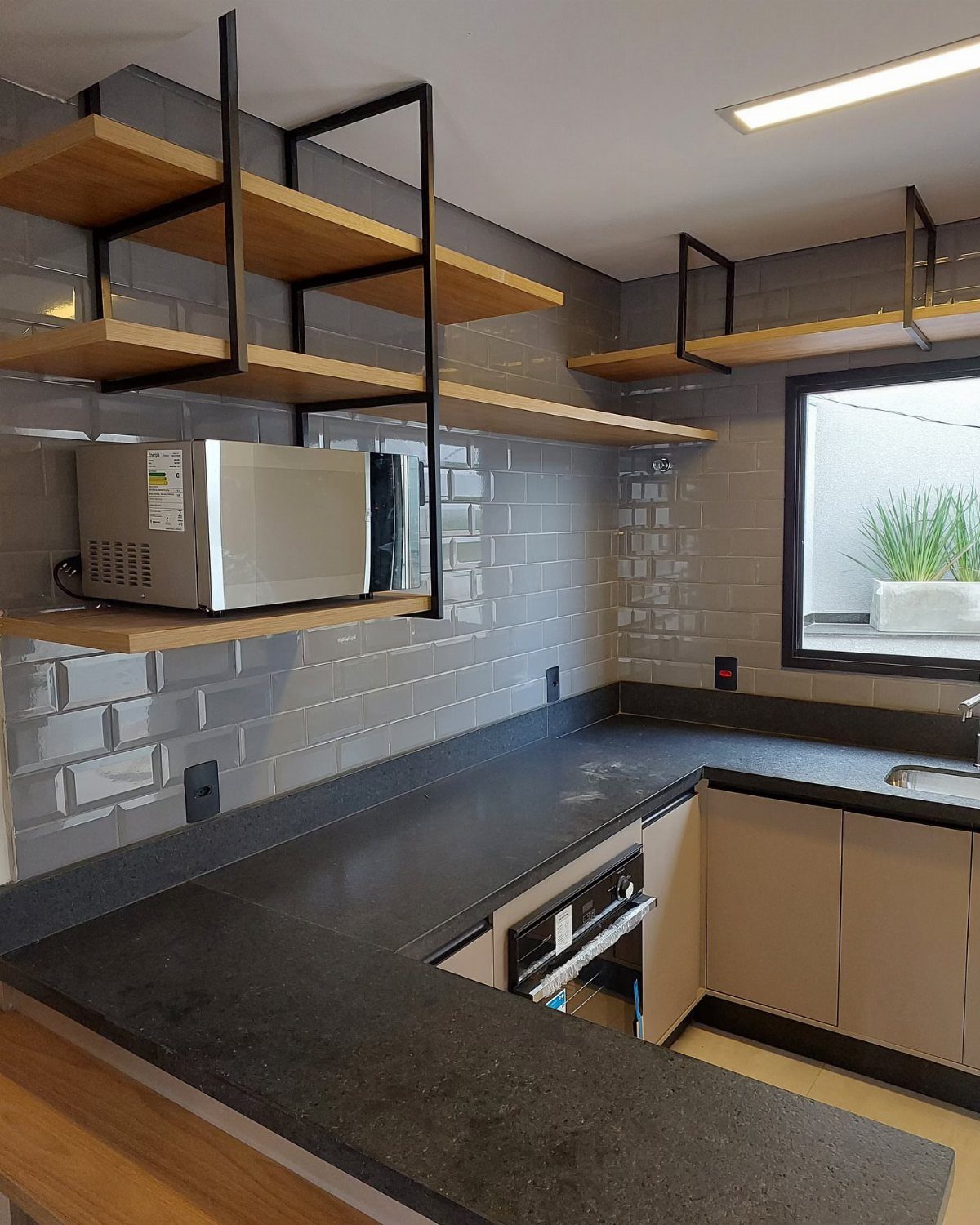 Wooden open shelves with black metal frames mounted on a grey subway tile backsplash in a kitchen.