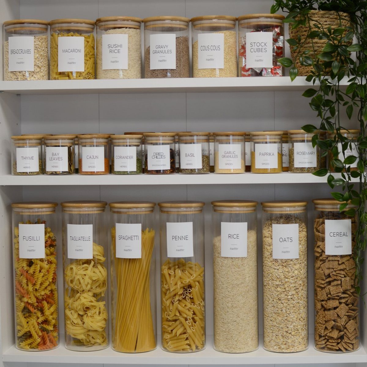 Clear glass jars filled with various dry pantry goods arranged on white open shelves.