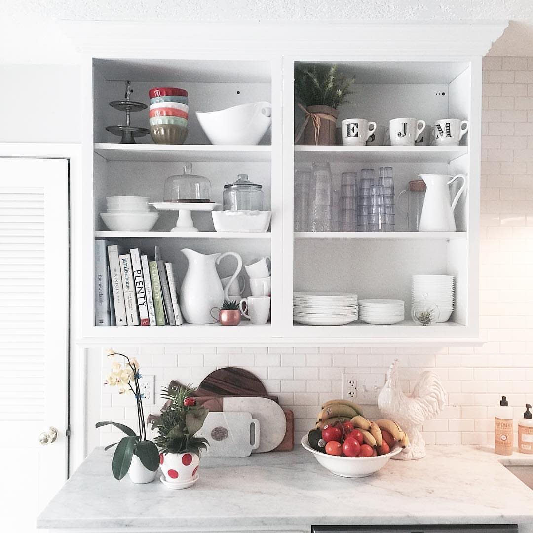 White built-in shelves displaying various white ceramic dishes, pitchers, and bowls in a bright kitchen.