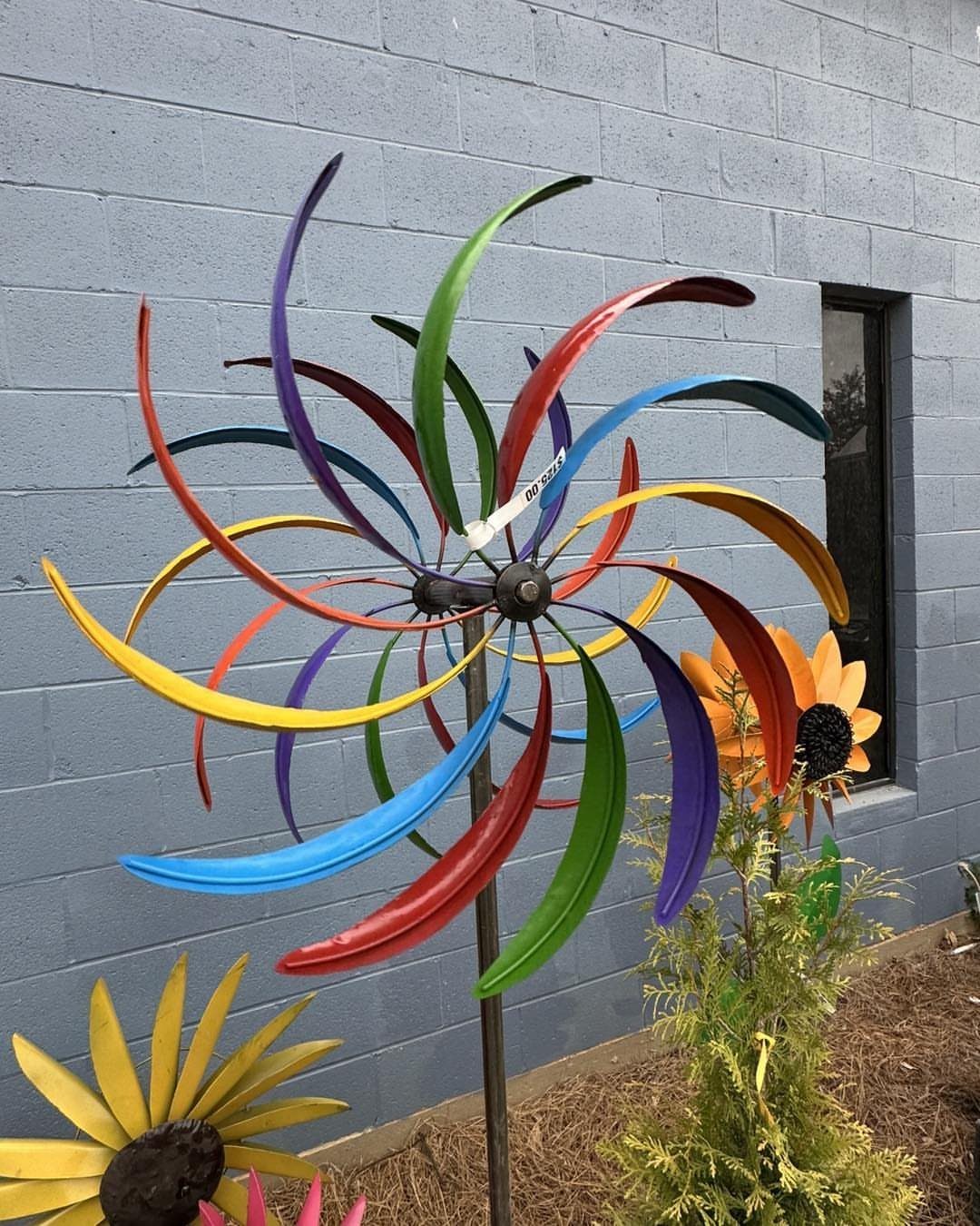Metal Yard Art Ideas for Your Garden in 7 Styles 6 A colorful metal wind spinner with curved blades in various bright colors standing in a garden.