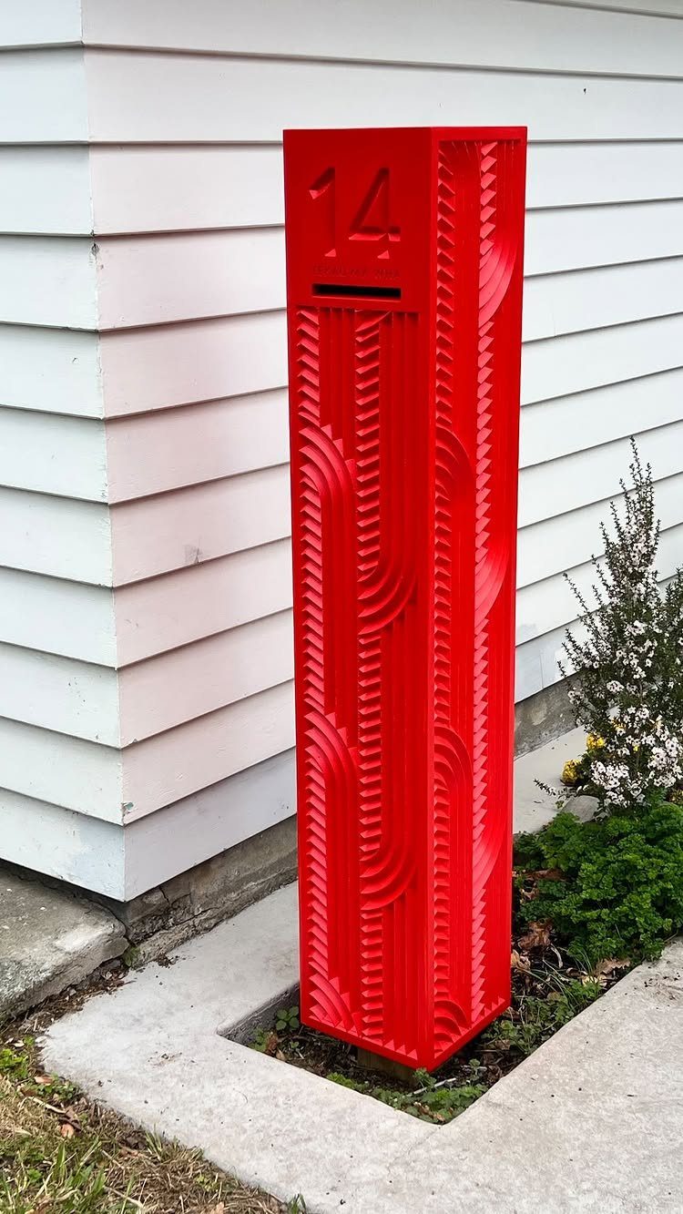 Metal Yard Art Ideas for Your Garden in 7 Styles 1 A tall, bright red textured metal letterbox with the number 14 standing next to a white house.