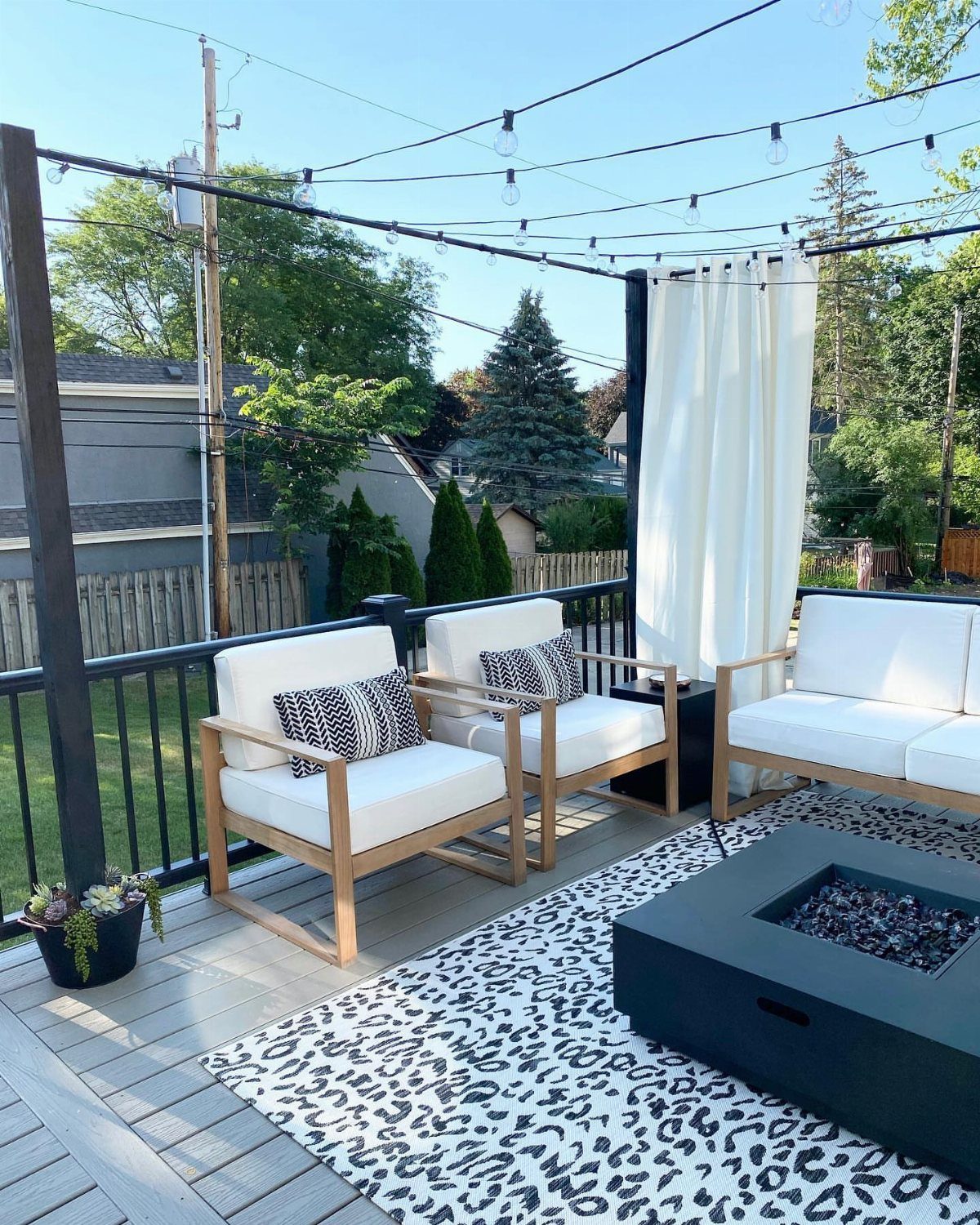 9 Modern Deck with Pergola Ideas for Living, Shade & Dining 4 White outdoor lounge chairs and a fire pit sit under string lights and white curtains on a deck.