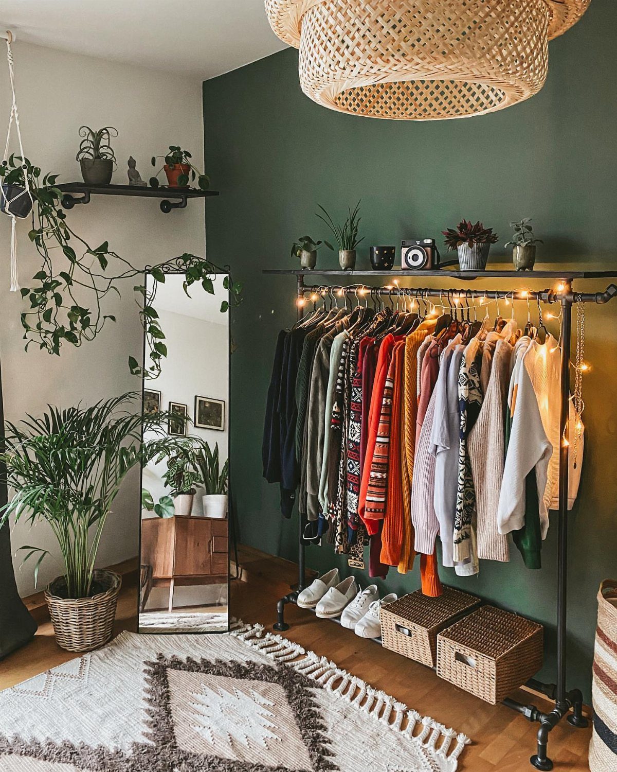 11 No Closet Room Ideas for Clothing Racks, Under-Bed Storage and More 1 A black metal pipe clothing rack filled with colorful clothes against a green wall.
