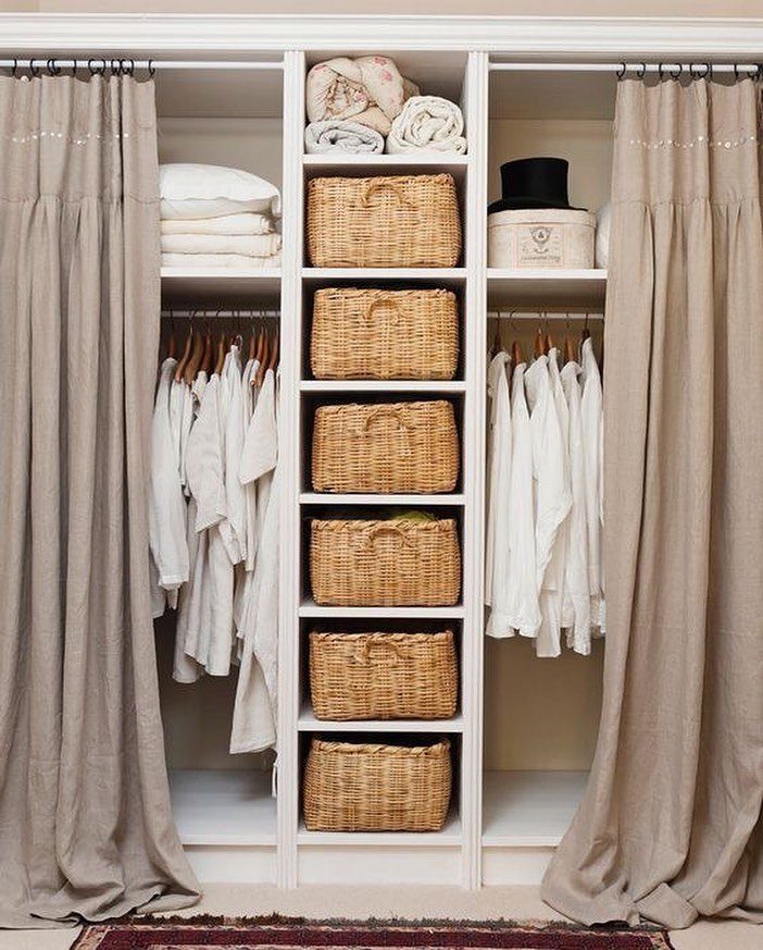 11 No Closet Room Ideas for Clothing Racks, Under-Bed Storage and More 5 Beige linen curtains partially covering white built-in shelving units filled with clothes and wicker baskets.