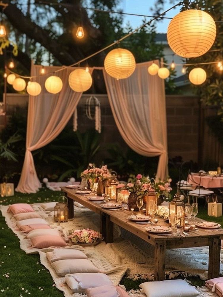7 Outdoor Lounge Area Ideas for Entertaining and Relaxing 3 A long wooden table set with flowers and candles on a lawn with lanterns.