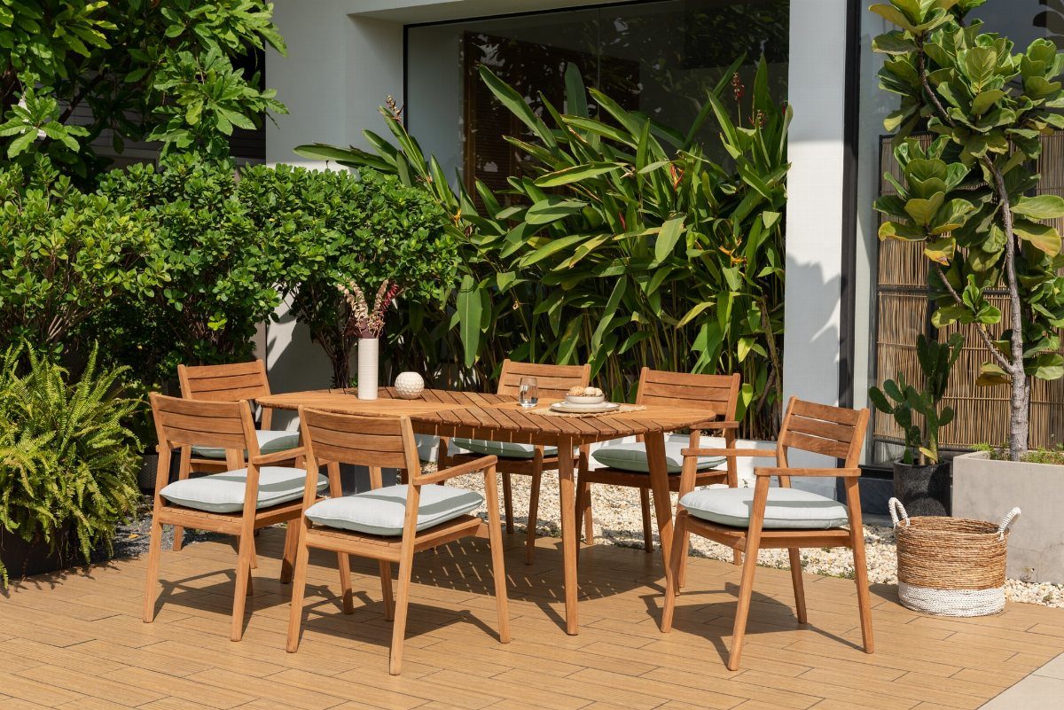Patio Dining Table and 7 Outdoor Eating Area Ideas 2026 1 Teak patio dining set with six chairs and blue cushions on a wooden deck.