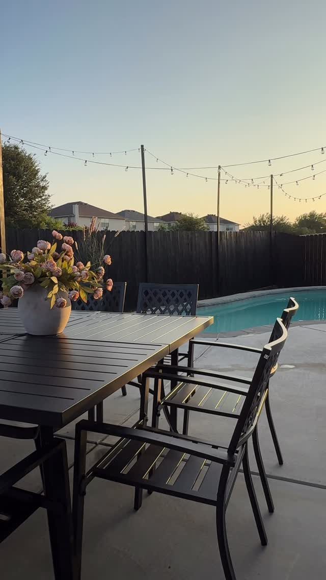 Patio Dining Table and 7 Outdoor Eating Area Ideas 2026 6 Dark metal dining table with floral centerpiece on a patio near a swimming pool.