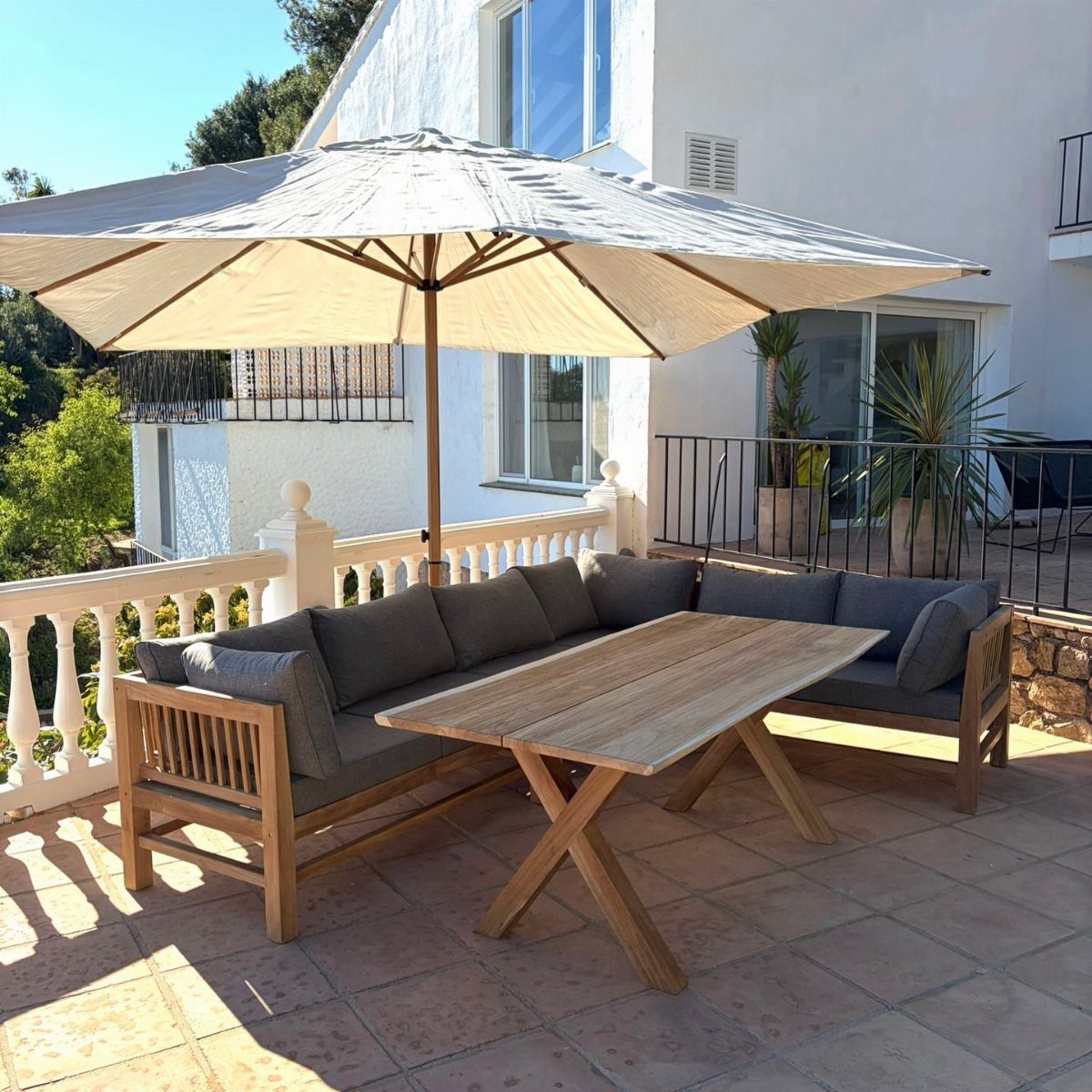 Patio Dining Table and 7 Outdoor Eating Area Ideas 2026 7 A wooden outdoor dining set with a rectangular table and L-shaped sofa under a large umbrella.