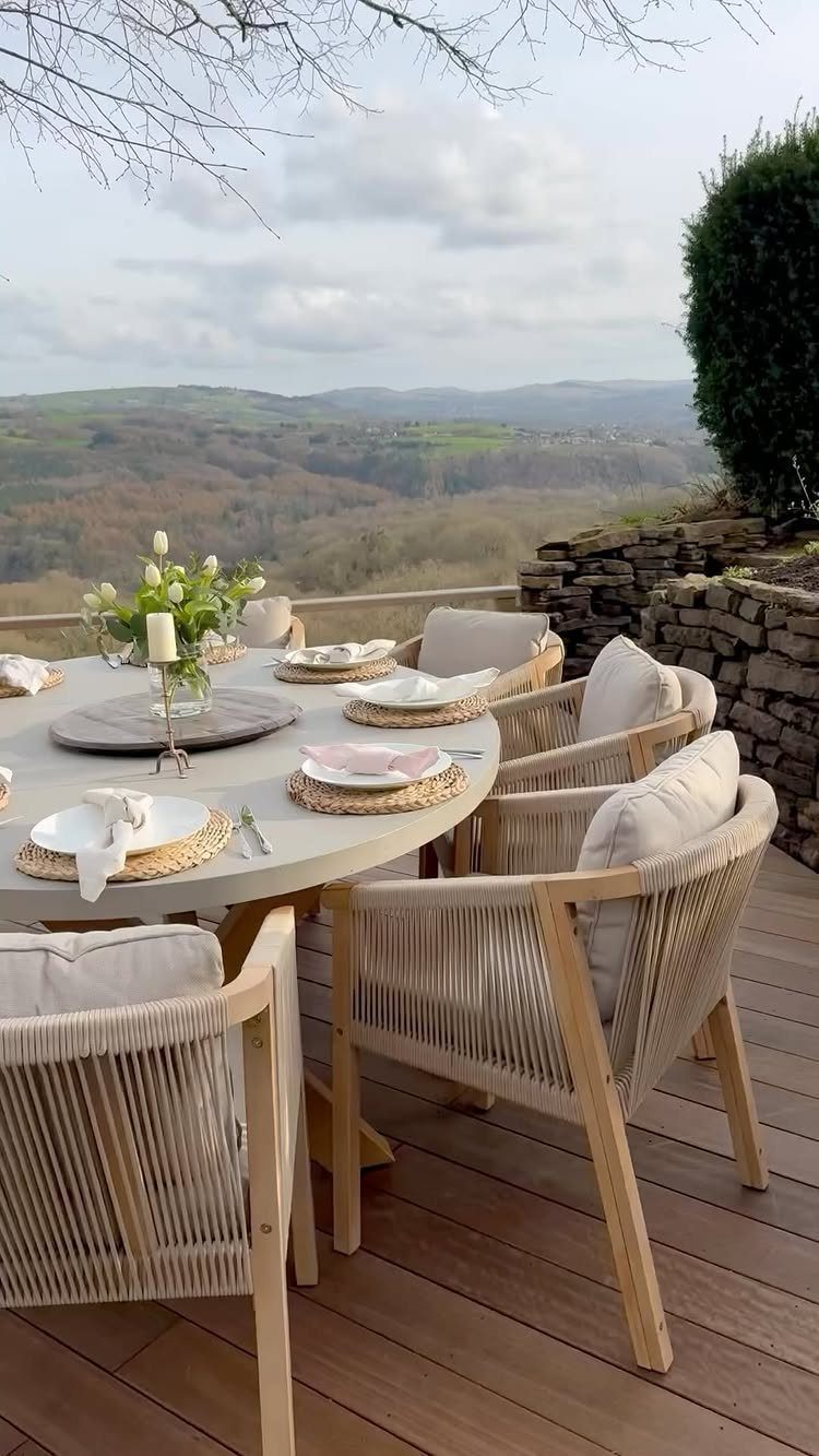 Patio Dining Table and 7 Outdoor Eating Area Ideas 2026 5 A round grey dining table with chairs set on a wooden deck overlooking a valley.