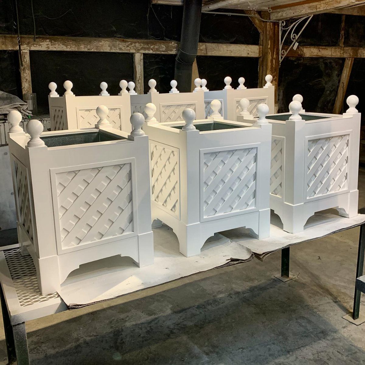 13 Planter Boxes Ideas for Your Porch, Deck and Garden 5 Four white wooden planter boxes with lattice side panels and spherical finials on a workbench.