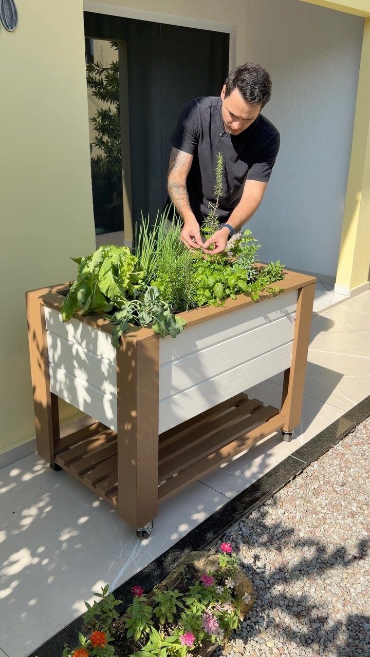 14 Raised Garden Bed Ideas for Cedar, Stone, Metal & More 14 A man tending to green plants inside a wooden raised garden planter on wheels.