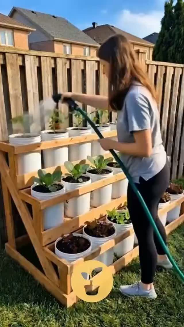 14 Raised Garden Bed Ideas for Cedar, Stone, Metal & More 3 A woman uses a hose to water plants in a wooden tiered vertical garden planter.