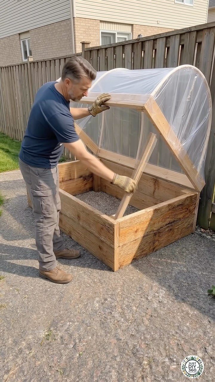 A man constructing a wooden raised garden bed with a clear plastic arched cover outdoors.