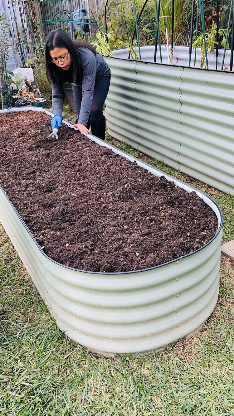 A woman tending to dark soil inside a corrugated galvanized metal raised garden bed.
