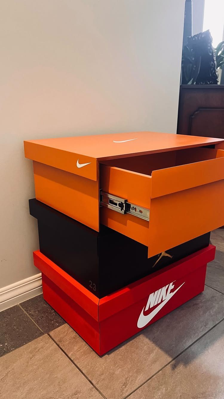 Stacked Nike shoe boxes in orange, black, and red on a tiled floor.