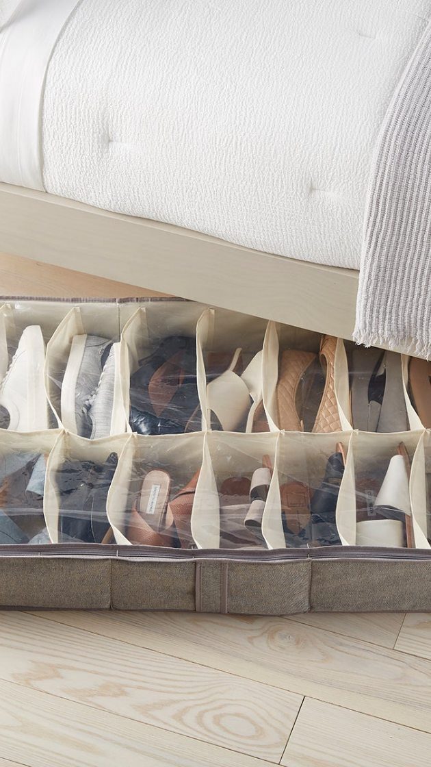 Clear plastic storage container filled with various shoes tucked under a white bed frame.