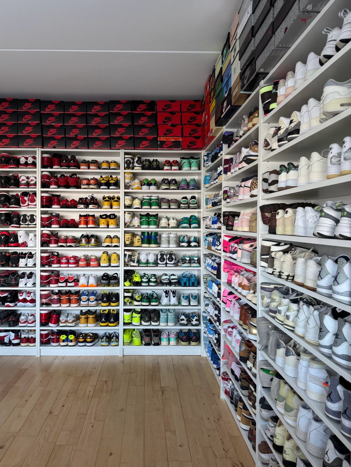 White shelving units filled with many colorful sneakers and red shoe boxes in a room.